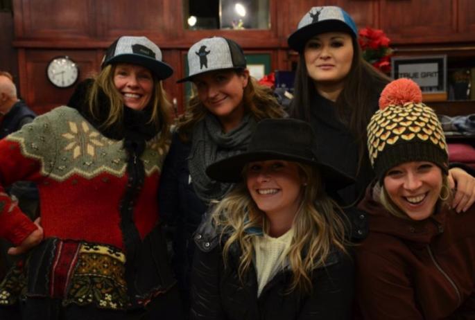 A group of women smiling wearing hats in a store.