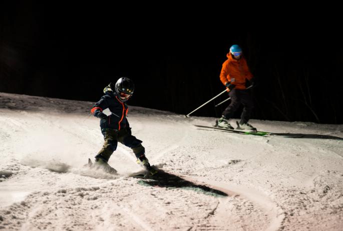 A father and son downhill ski under the night lights.