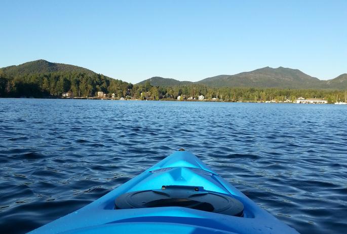 A blue kayak on the lake with multiple mountains in the background.