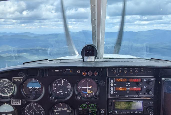 The view of airplane controls from the pilot's seat, with mountains beyond.