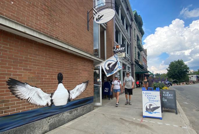 a couple walks past a loon mural on a clear day.