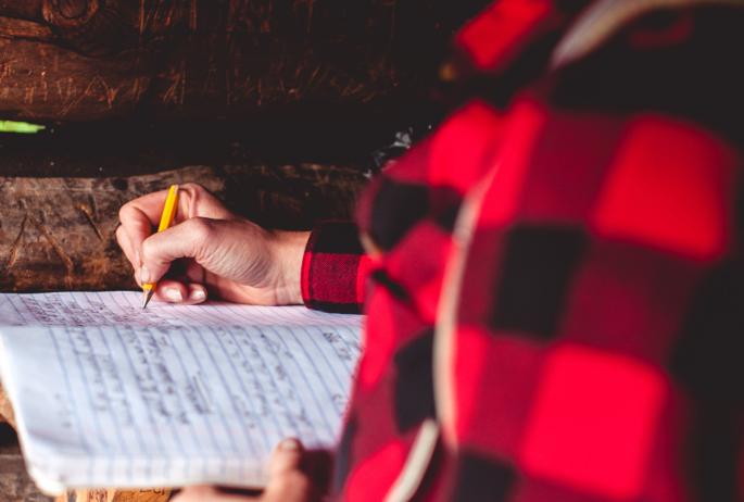 A person wearing a flannel writes in a notebook