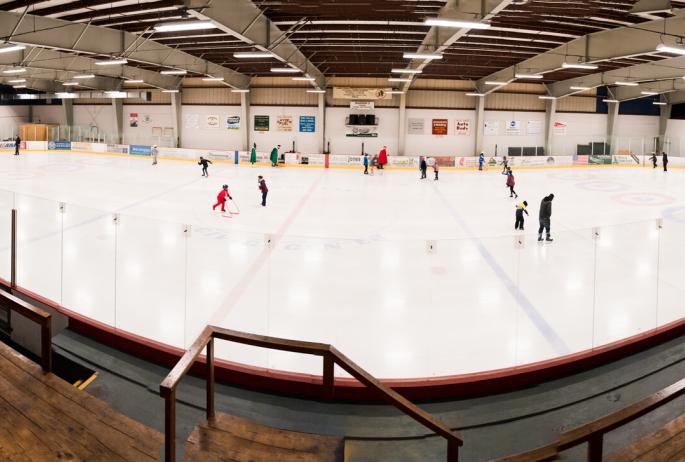 An ice rink as viewed from the bleachers. People are skating on the ice.