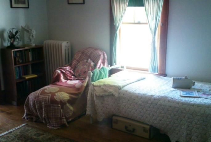 The bedroom of one of the cure cottages of Saranac Lake, complete with a bed, recliner, and ceramic jug used to keep feet warm at night known as a "pig"