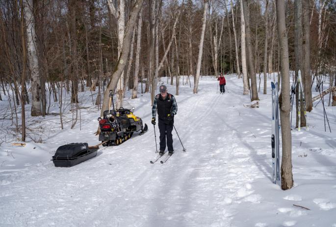 A skier passes a snowmobile on a snowy trail
