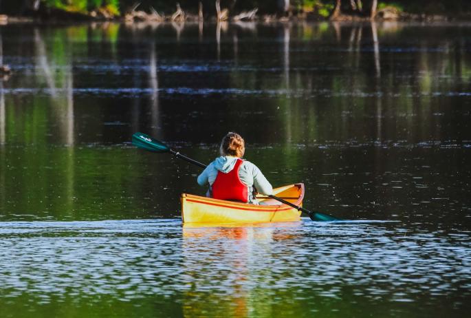 A woman in a solo pack canoe paddling with a green paddle