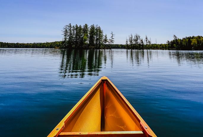 The bow of a canoe on a placid pond with two small islands directly in front.