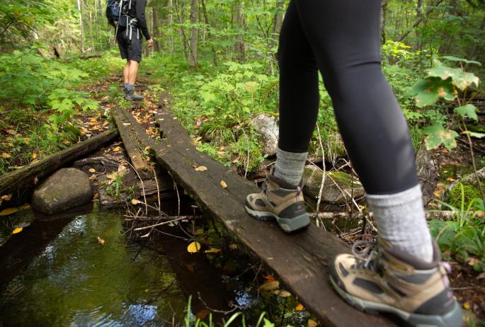 A view of two hiker's boots as they walk across a wooden plank bridge