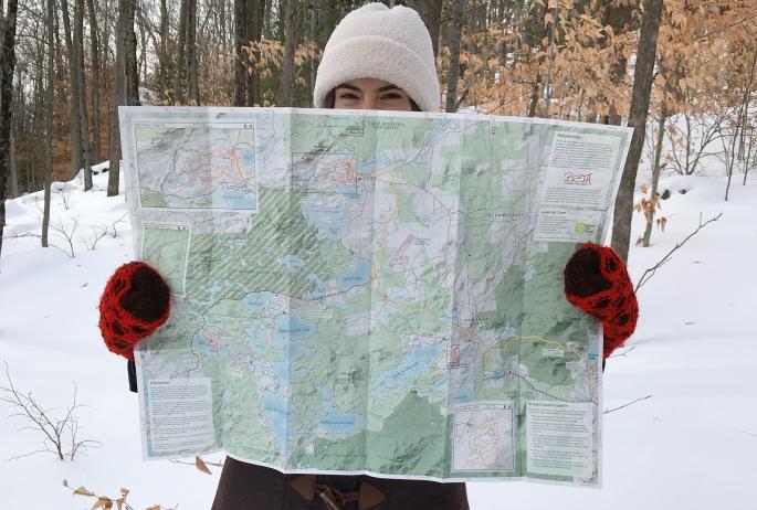 A woman holds up a map in the snow.