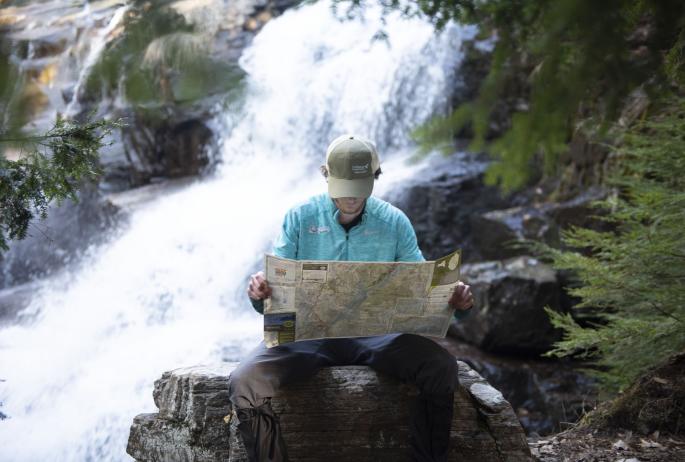 A man looks at a map in front of a waterfall
