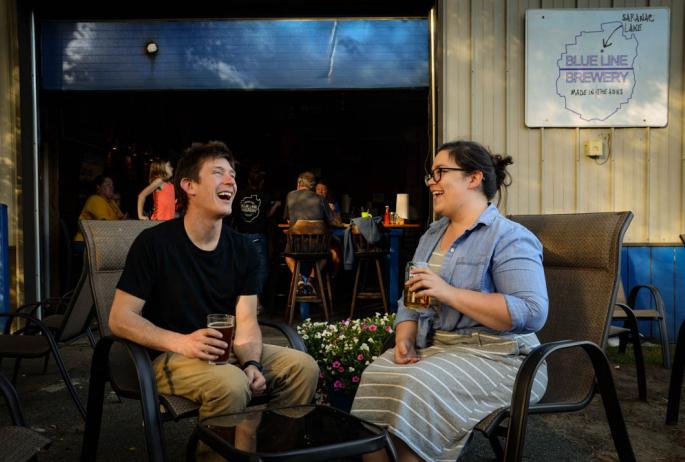 Two people laugh while enjoying beer outside a brewery