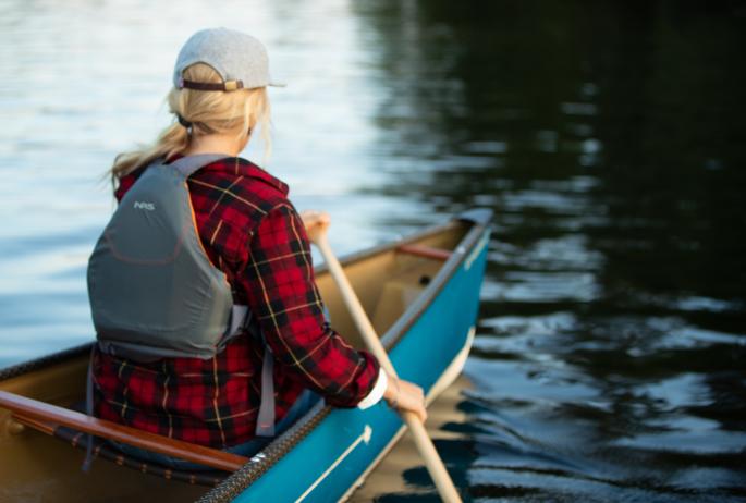 A woman paddles in the front position of a canoe