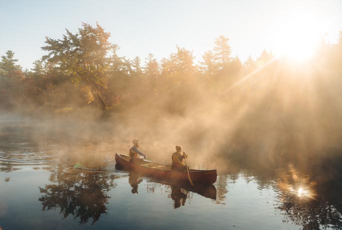 A man and woman paddle through morning mist.