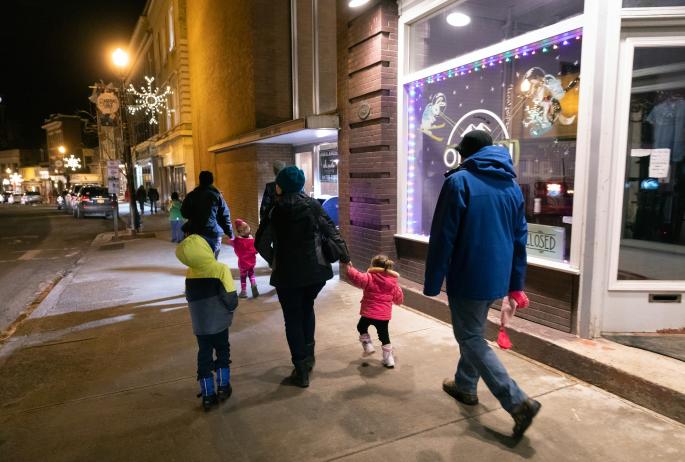 A family walks down a sidewalk with shops in winter.