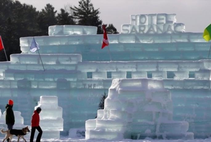 Two people walk by a castle made of ice in winter.