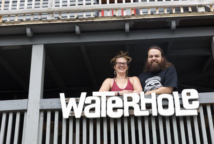 Two people on a balcony with a sign for Waterhole