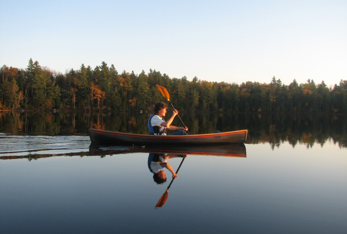 A person canoeing on a glassy lake during fall.