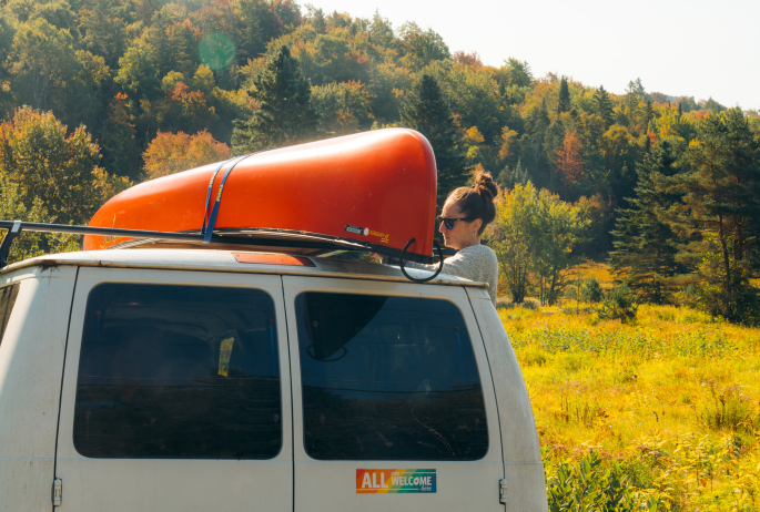 A woman putting a canoe on top of her car.