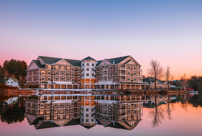A sprawling hotel sits on the edge of a lake in early winter with the sun rising in the background.