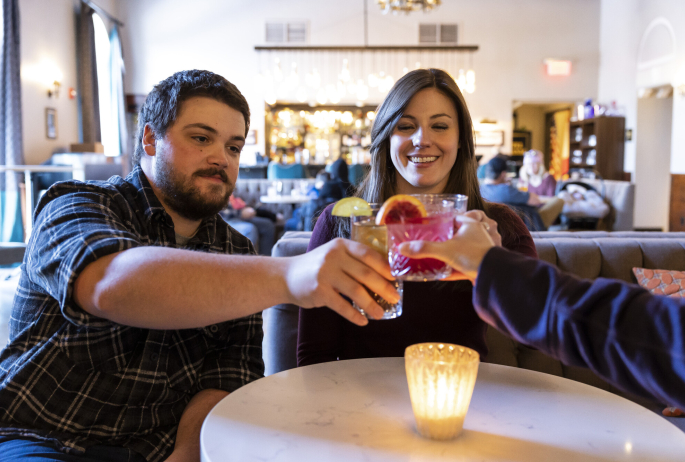 Three friends cheers cocktails together at a brightly lit restaurant.