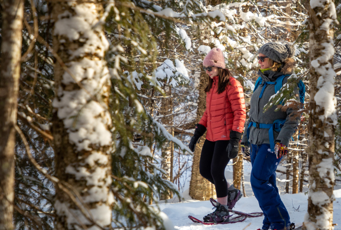 Two women snowshoeing on a snowy trail.