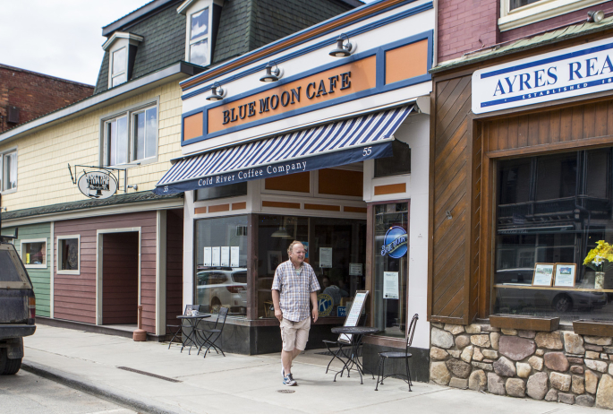 A man walks out of a cafe onto a main street.