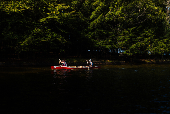 Two people paddle in  a canoe on a river in summer.