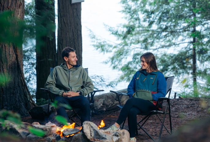 A man and woman sit in chairs by a fire pit.