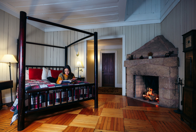 A woman reads a book on a bed in a cabin.