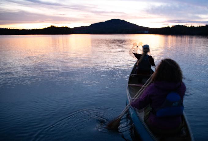 Two people canoeing towards the sunset on Lower Saranac Lake