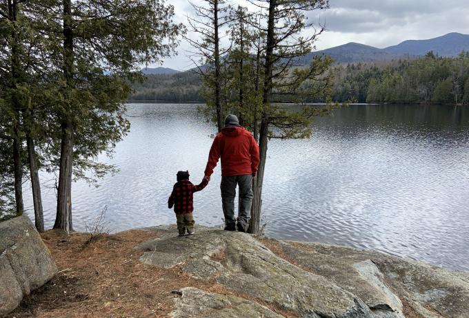 Father and son hold hands as they walk over a rock near the shoreline of Moose Pond
