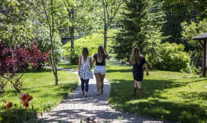 Three girls walk along the stone path of the Saranac Lake Riverwalk on a beautiful summer day.