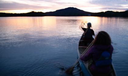 Two people canoeing towards the sunset on Lower Saranac Lake