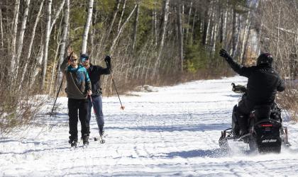 Snowmobilers wave to xc skiers on a snowy trail