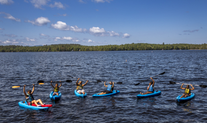 A group of kayakers hold their paddles above their heads in triumph.