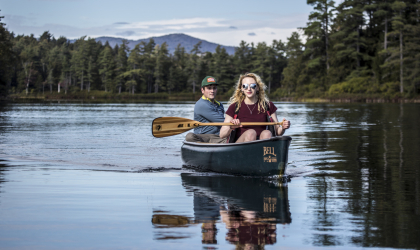 Two people canoeing on a lake surrounded by trees