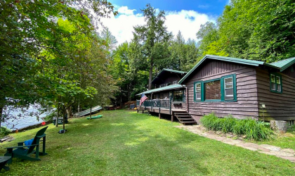 Lush green lawn next to blue waters of Lake Flower highlight the dark stain on this Log cabin by the lake.