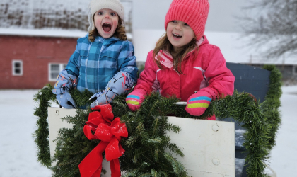 Two very happy young girls in a sled with garland and wreaths with red bows.